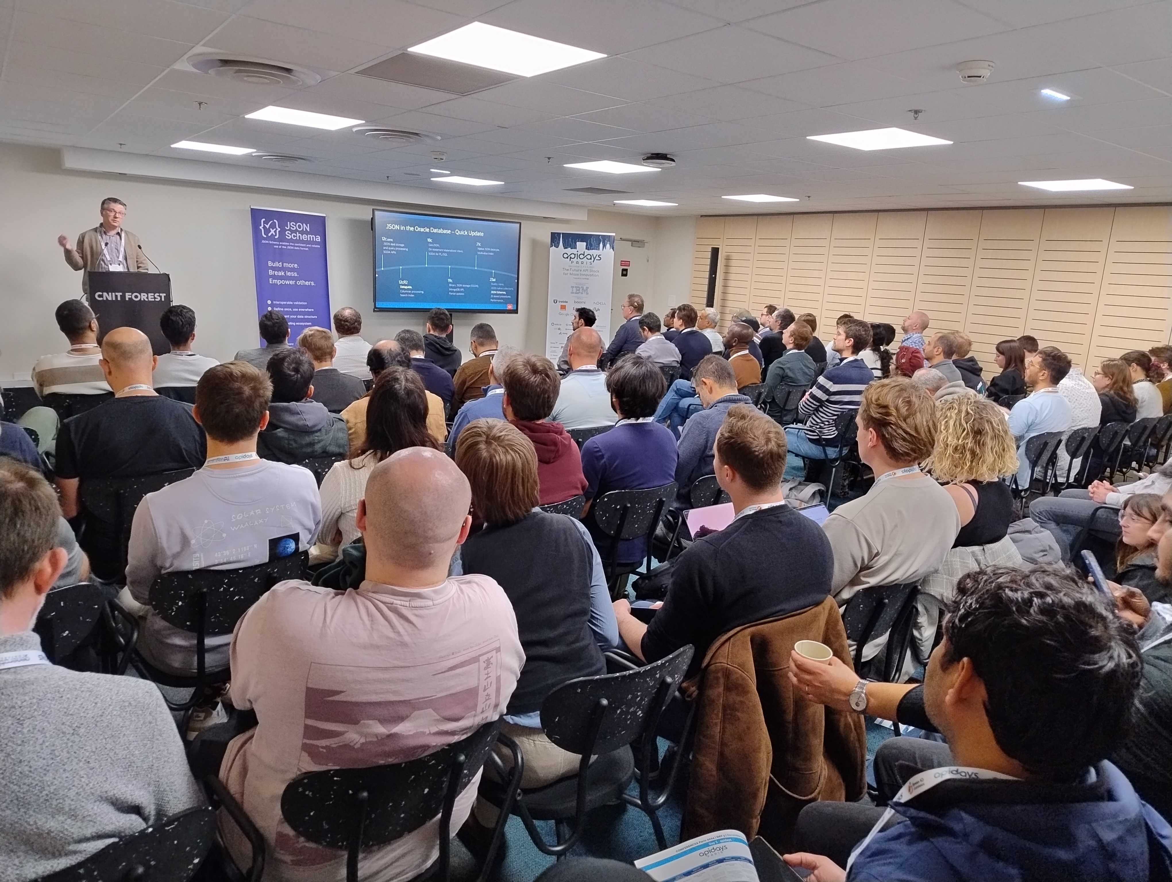 Loic Lefevre presenting on stage at the APIDays Paris 2024 conference. The audience is seated in rows of chairs, facing the stage.